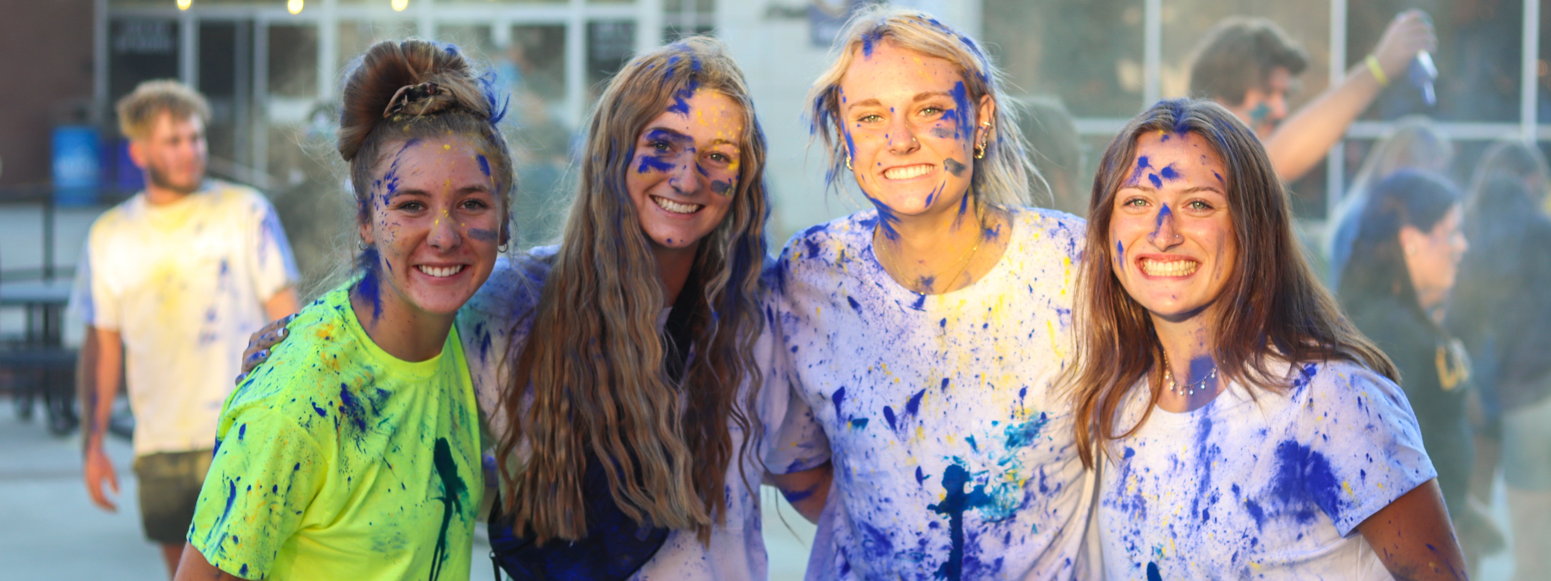 Communications Photo Header: Central girls standing together smiling, covered in blue color powder