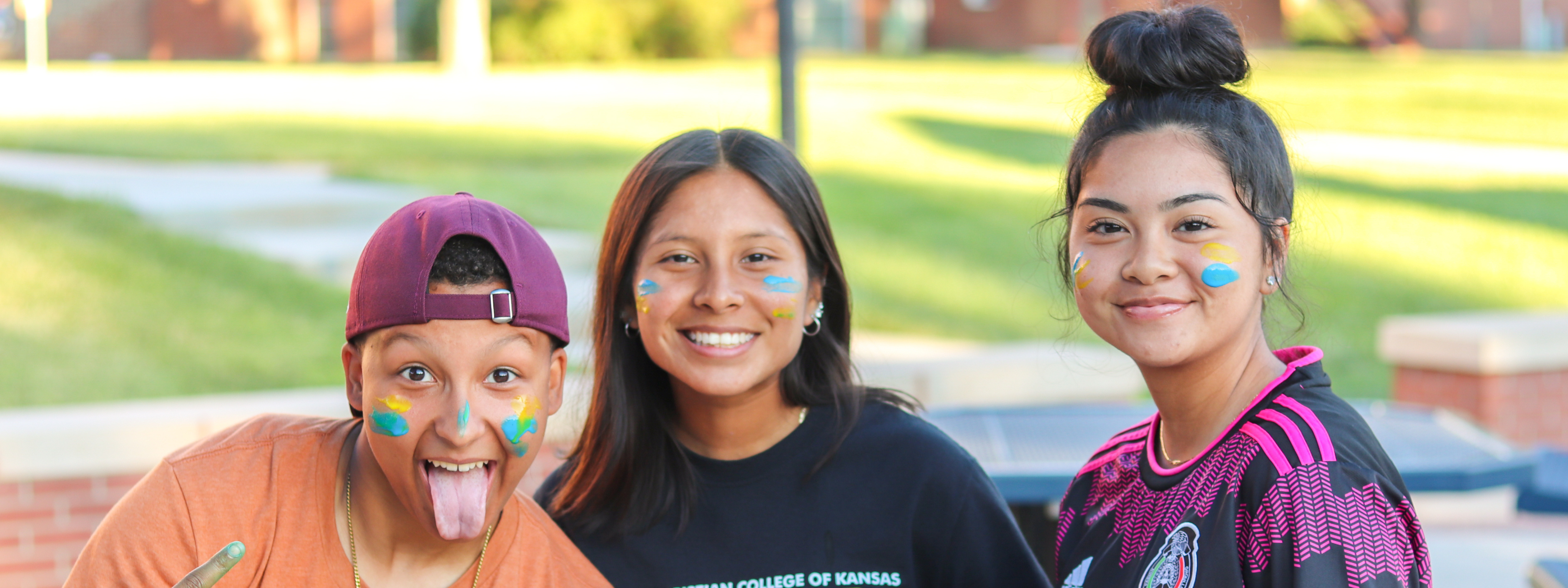 Human Services Photo Header: Central girls posing and smiling in the plaza with blue and yellow face paint