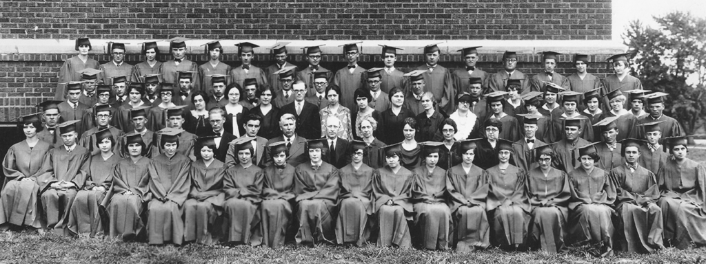 Group of graduates in chairs outside of a brick building with President and Mrs. Stoll